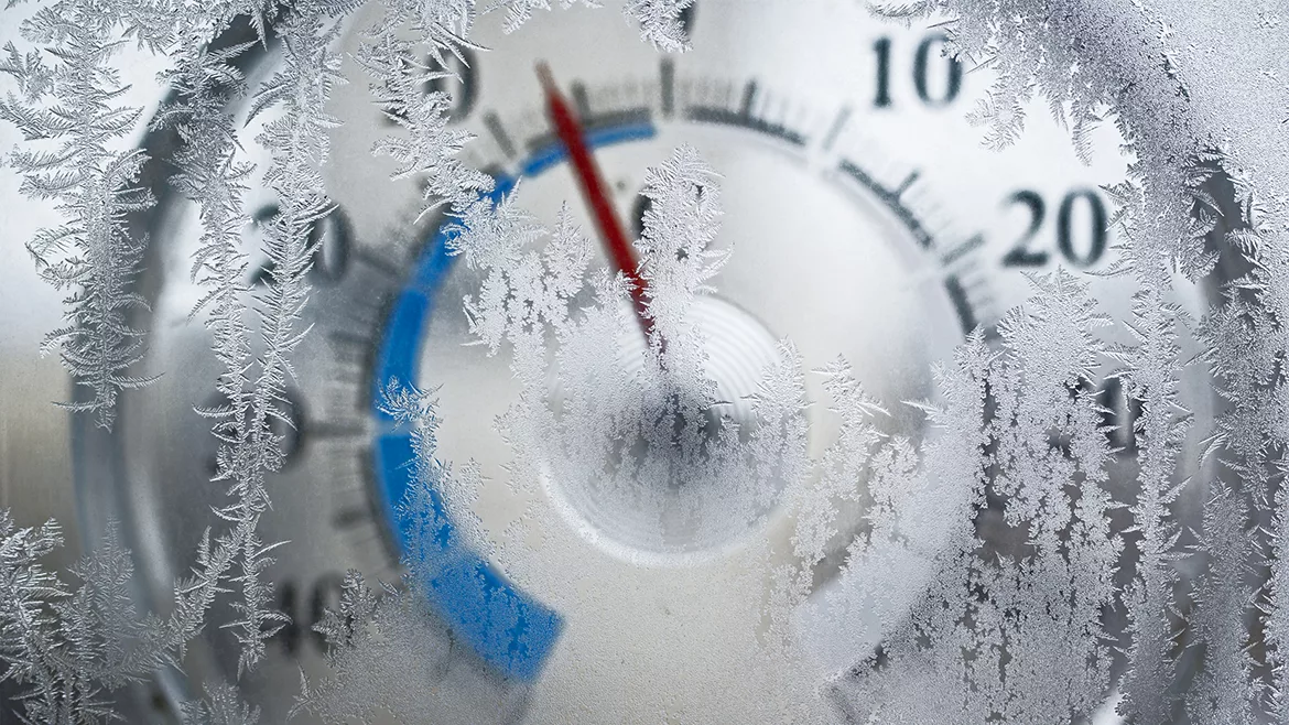 Thermometer for icy window shows the temperature of - 6 degrees Celsius. Red arrow on a blue field. The image is slightly blurry. Frost on the window in focus.
