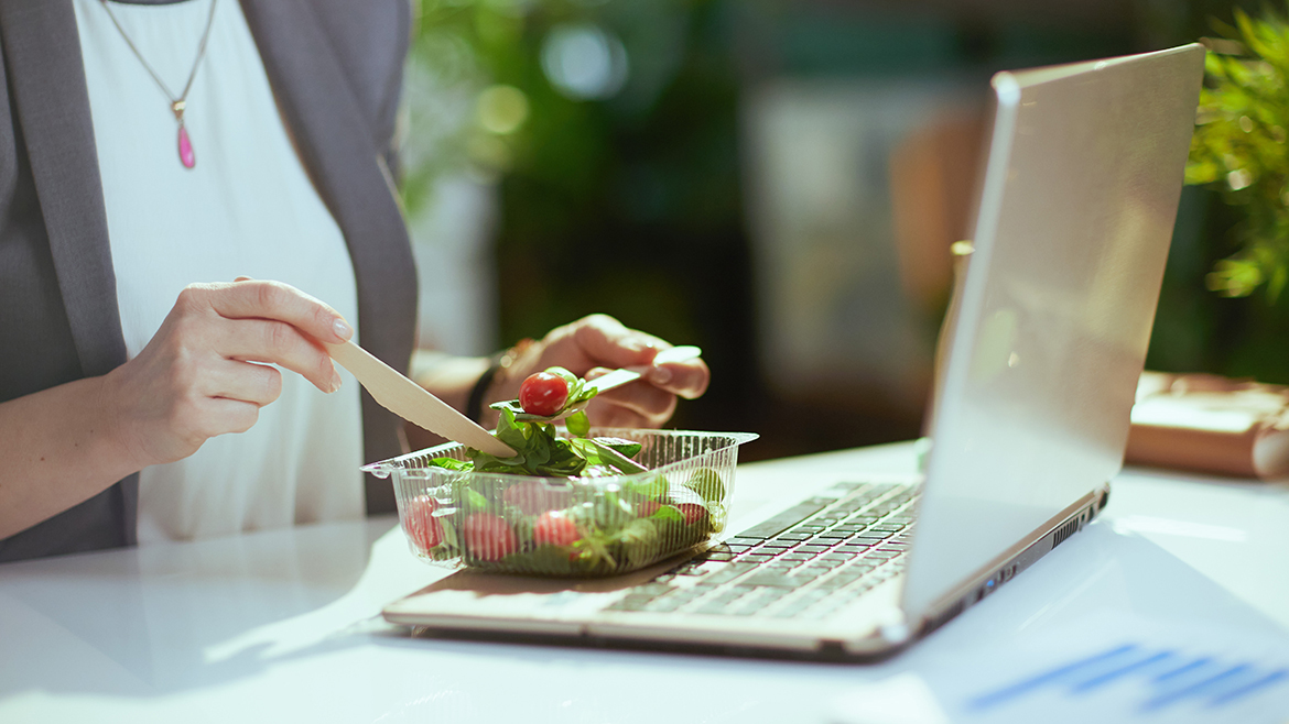 Woman eating salad with laptop