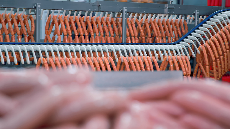 Sausages hanging on racks in an automated production line within a meat processing plant.