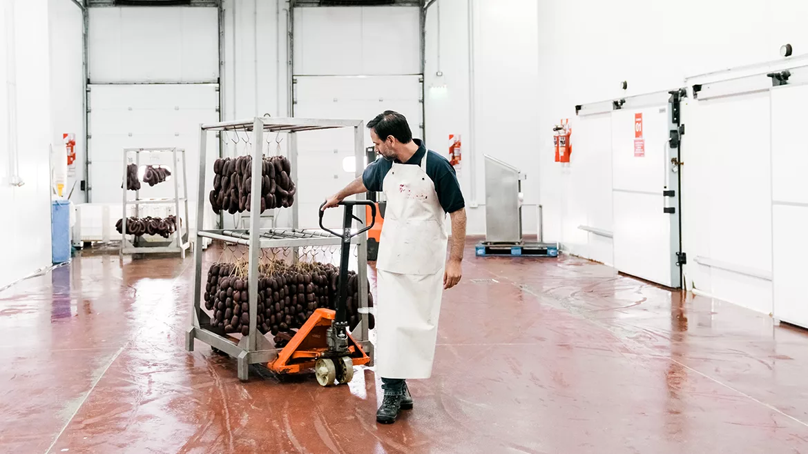A male butcher is moving sausages on a pallet jack in a food processing plant.