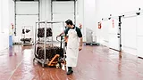 A male butcher is moving sausages on a pallet jack in a food processing plant.