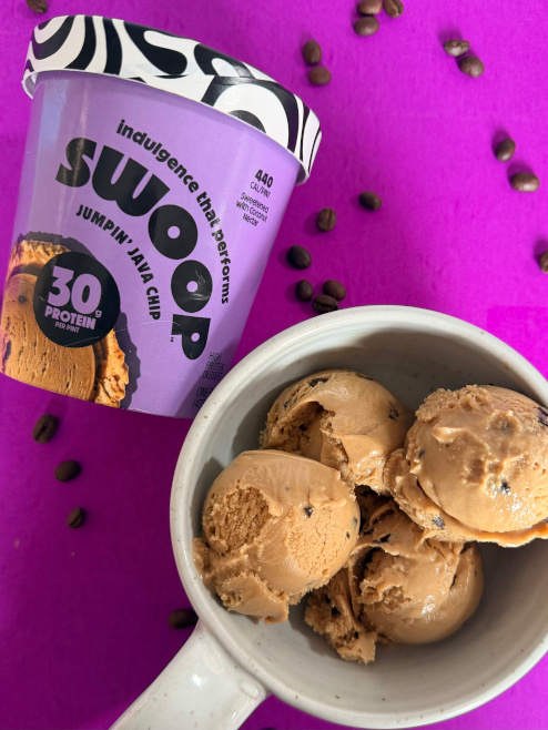 An overhead view of a tub of Swoop Jumpin' Java Chip beside a bowl with four scoops.