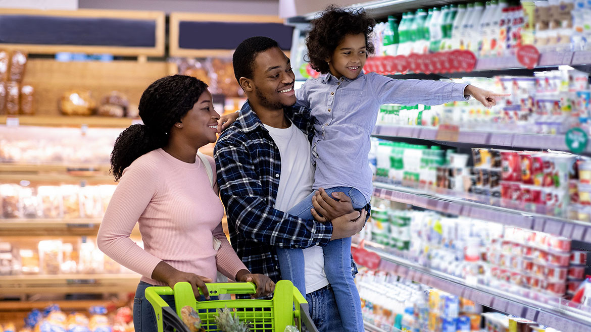 African American parents with lovely daughter buying food at supermarket.