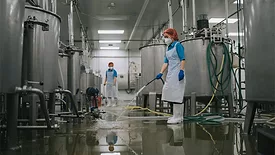 Factory worker cleaning near storage tanks and filtering machines after production is completed.