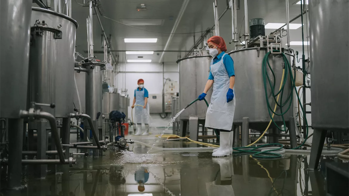Factory worker cleaning near storage tanks and filtering machines after production is completed.