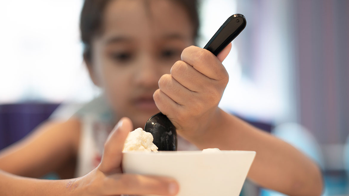 A little girl eating ice cream with a spoon. The girl is blurred in the background.