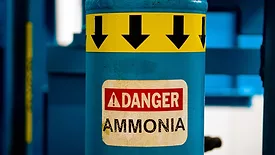 Blue ammonia gas cylinder that has a yellow band at the top with black arrows pointing down and a "Danger Ammonia" sticker.