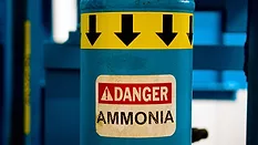 Blue ammonia gas cylinder that has a yellow band at the top with black arrows pointing down and a "Danger Ammonia" sticker.