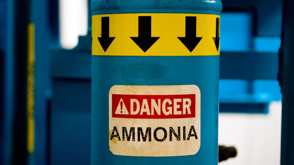 Blue ammonia gas cylinder that has a yellow band at the top with black arrows pointing down and a "Danger Ammonia" sticker.